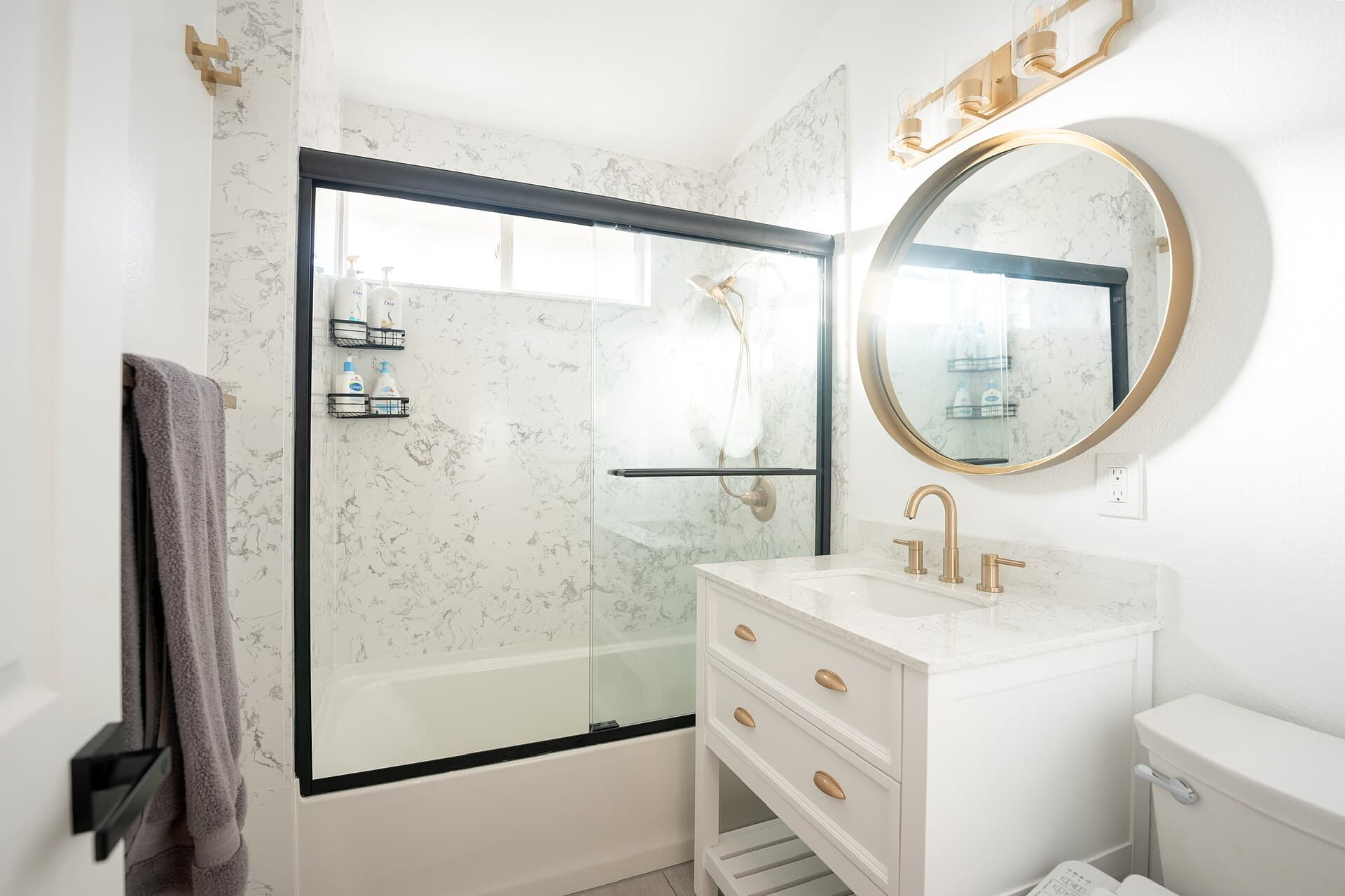 Remodeled bathroom with marble walls, black-framed glass, and gold fixtures