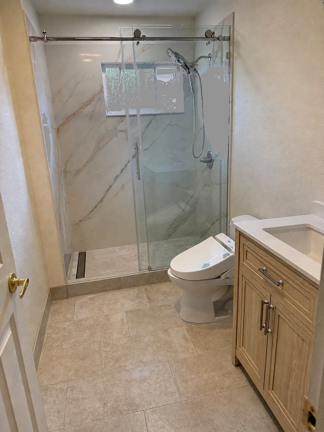 Remodeled walk-in marble shower with frameless glass and light oak vanity